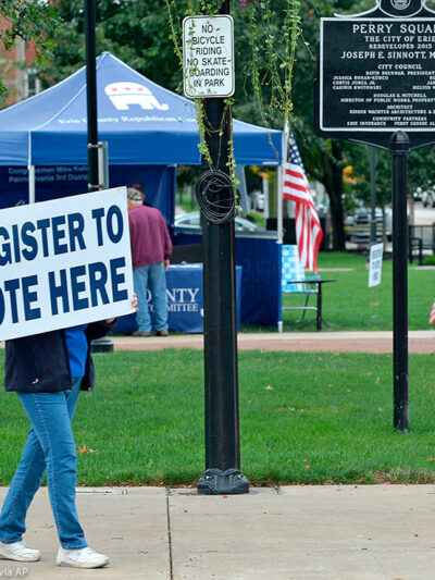 Person holds sign that reads "register to vote here" near a voter registration booth on a Pennsylvania street