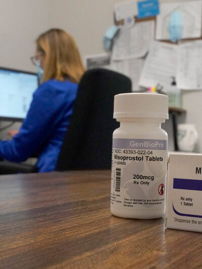 A box of the drug mifepristone pictured in front of a women on a computer.