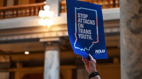 Inside the Indiana statehouse, a hand holds up a protest poster that reads, "stop attcks on trans youth"