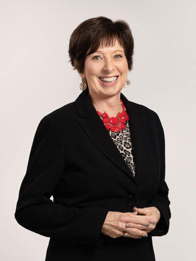 Coach McGraw poses for a headshot in a black blazer and red necklace.