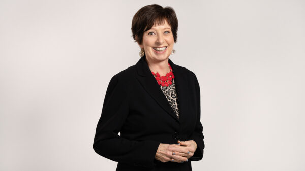 Coach McGraw poses for a headshot in a black blazer and red necklace.
