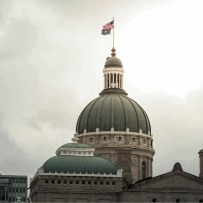 A photograph of the Indiana Statehouse rotunda. The sky behind the building is cloudy and gray.