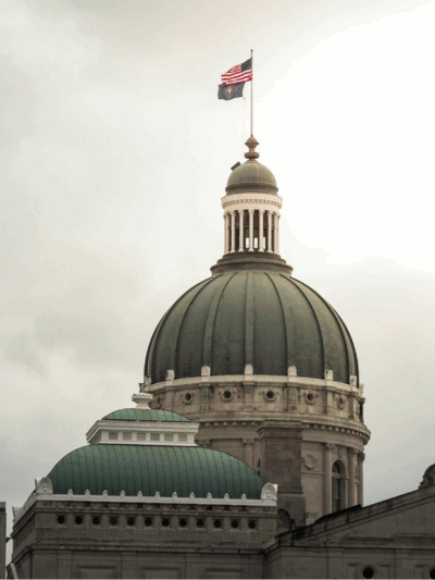 A photograph of the Indiana Statehouse rotunda. The sky behind the building is cloudy and gray.