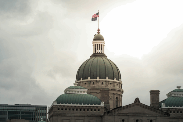 A photograph of the Indiana Statehouse rotunda. The sky behind the building is cloudy and gray.
