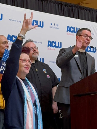 A crowd of people standing in front of a banner that features the ACLU of Indiana logo.