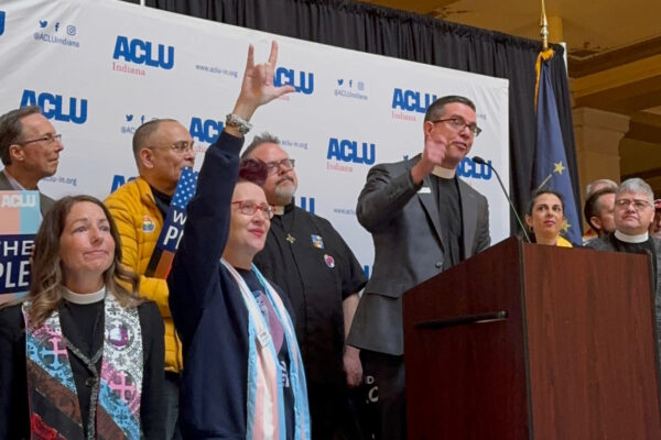 A crowd of people standing in front of a banner that features the ACLU of Indiana logo.