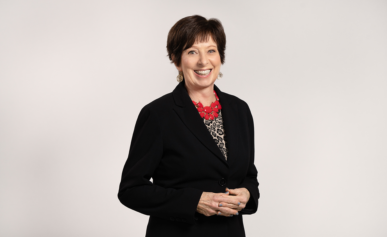 Coach McGraw poses for a headshot in a black blazer and red necklace. 