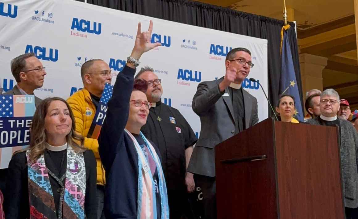 A crowd of people standing in front of a banner that features the ACLU of Indiana logo. 