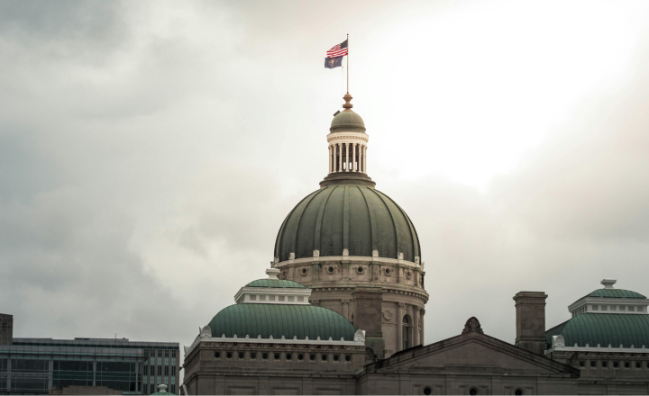 A photograph of the Indiana Statehouse rotunda. The sky behind the building is cloudy and gray.