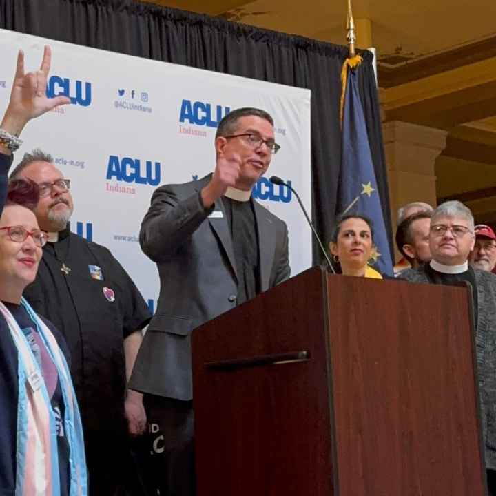 A crowd of people standing in front of a banner that features the ACLU of Indiana logo.